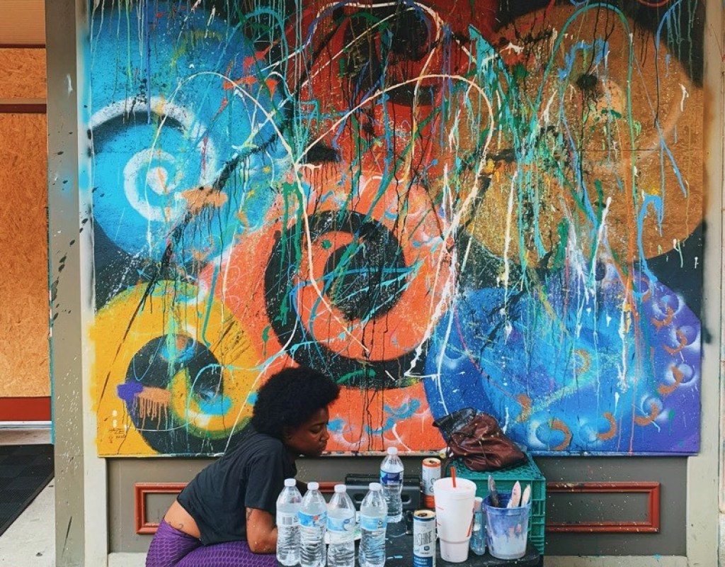 An artist in front of an abstract mural of swirling forms, drips, and slashes