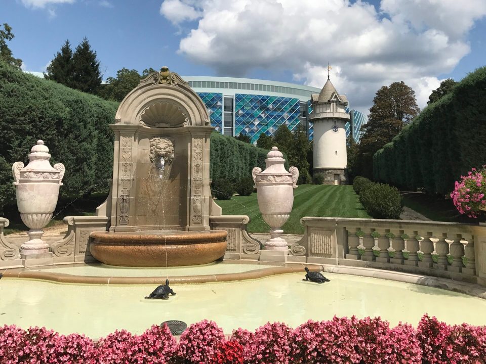 Behind a grand, antique-looking fountain is a modern hospital facade