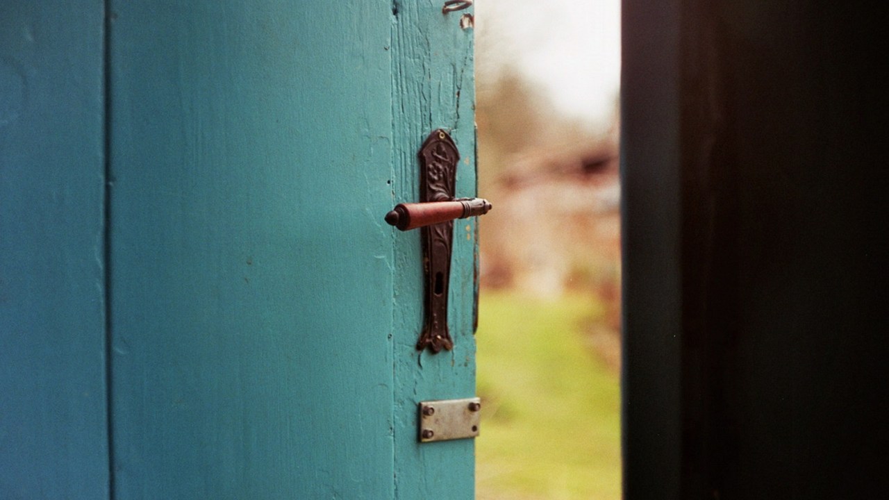 An door open just a crack reveals a green landscape beyond.