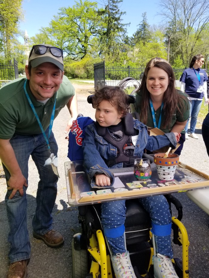 Two museum staff people in uniform posing with a patient in a wheelchair with a craft activity