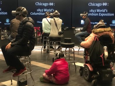 Participants wearing VR headsets in a room with screens reading "Chicago 00: 1893 World's Columbian Exposition"
