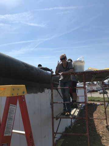 A student posing in front of the wall as it's being painted