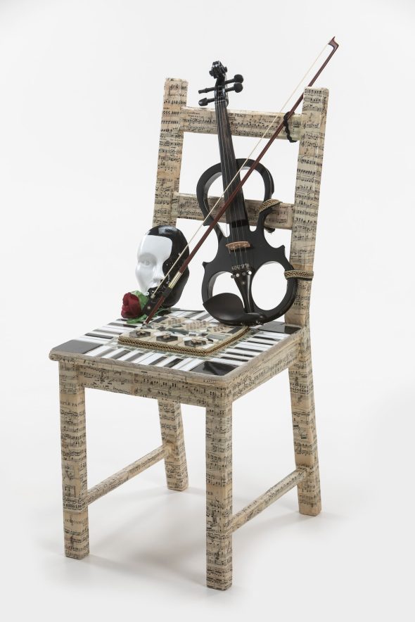 A chair wrapped in a sheet music print with a violin, opera mask, and rose on top