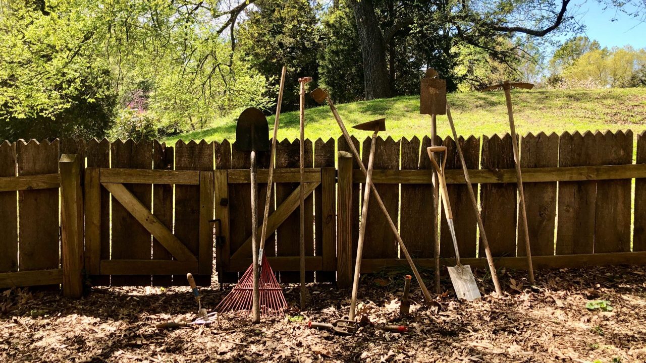 A fence with yard tools propped up against it