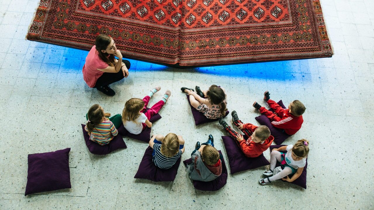An educator speaking to a group of children seated around a museum textile artifact