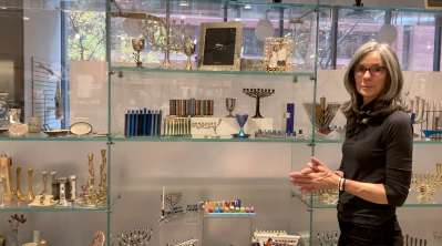 A woman standing in front of an array of ritual merchandise like menorahs inside a museum store