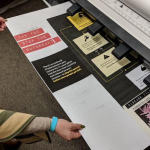 Person in green pulling large poster paper out of printer