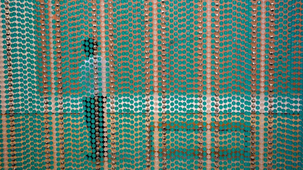 A visitor standing in a gallery looking at a painting seen through a colorful bead curtain