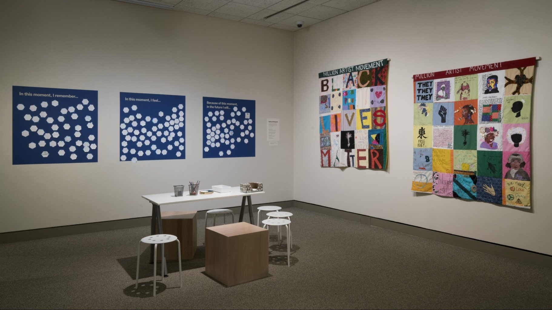 A museum gallery space with Black-Lives-Matter-themed art and a workstation for answering questions on poster boards: "In this moment, I remember...," "In this moment, I feel...," and "Because of this moment, in the future I will..."