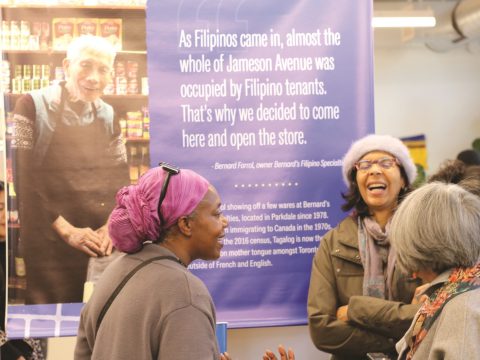 Several women stand smiling and laughing in front of an exhibition banner.