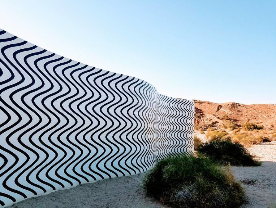 A curving wall with black squiggles against a white background in a desert setting