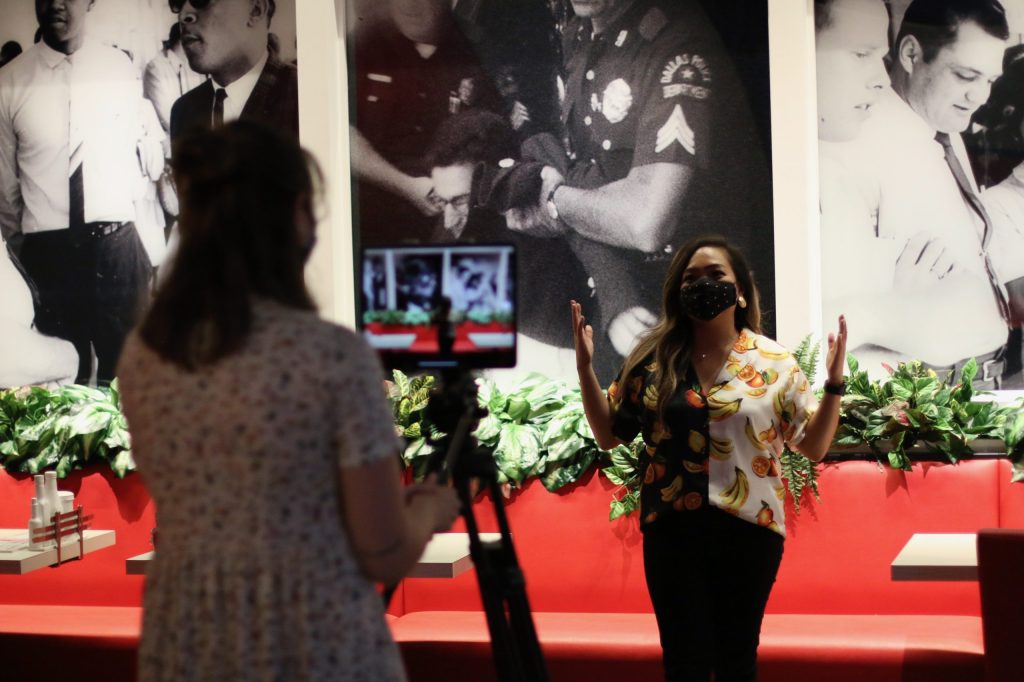 An educator speaking in front of a camera inside of a museum space