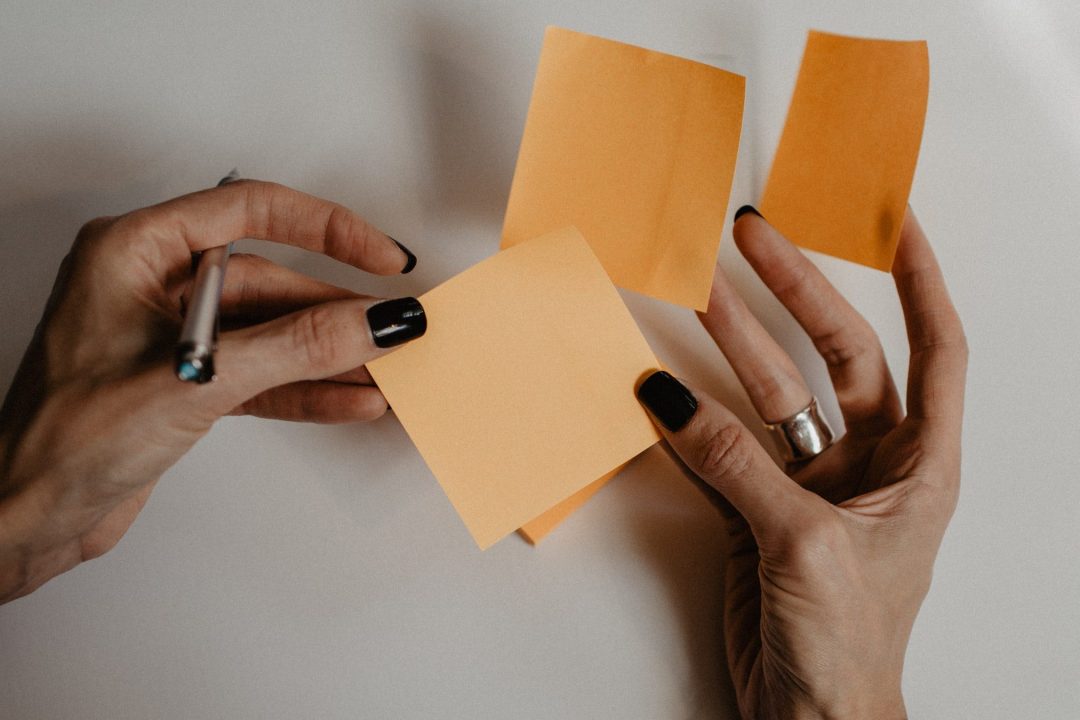 A pair of hands holding a set of sticky notes and a pen