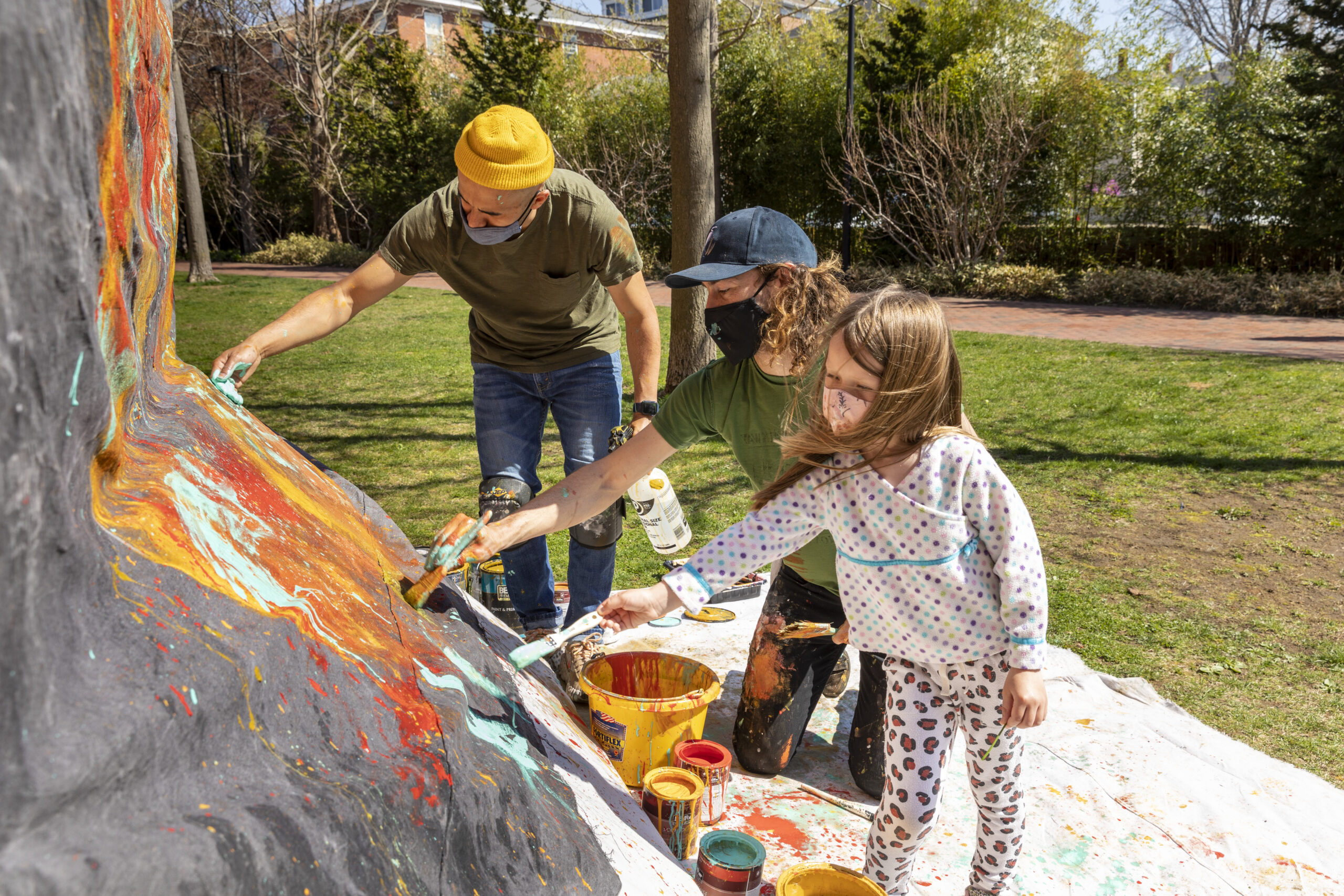 Two adults and one child outside painting bring colors onto a rock