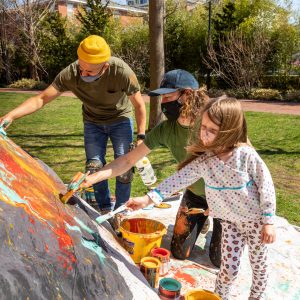 Two adults and one child outside painting bring colors onto a rock