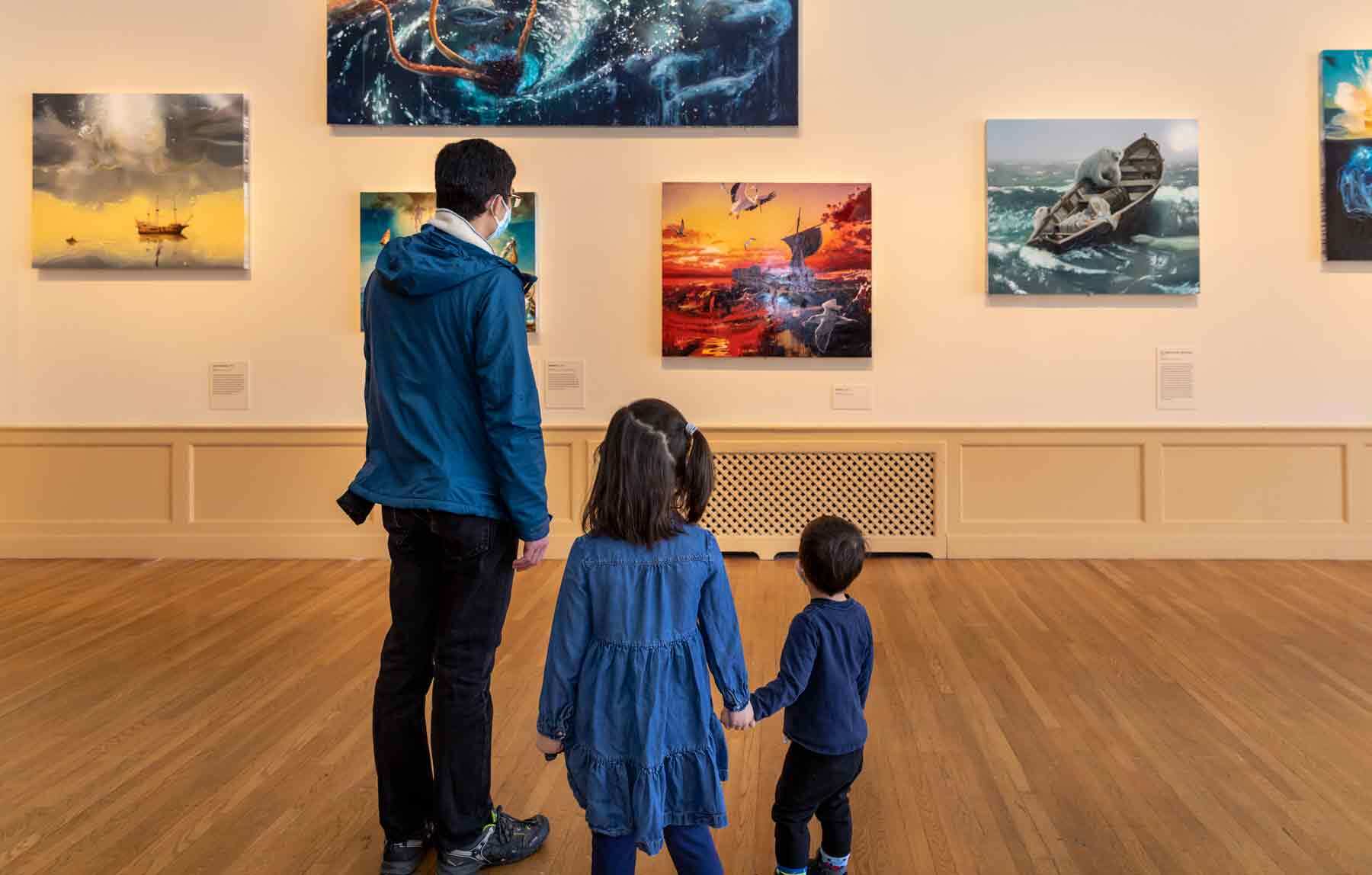 One adult and two children visitors looking at a gallery wall of paintings depicting fantastical shipwrecks