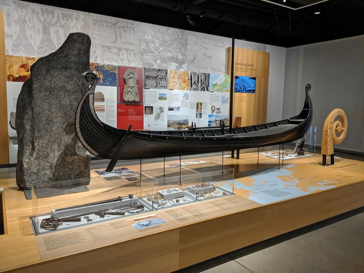 A museum gallery with a ship and several vitrines containing smaller objects