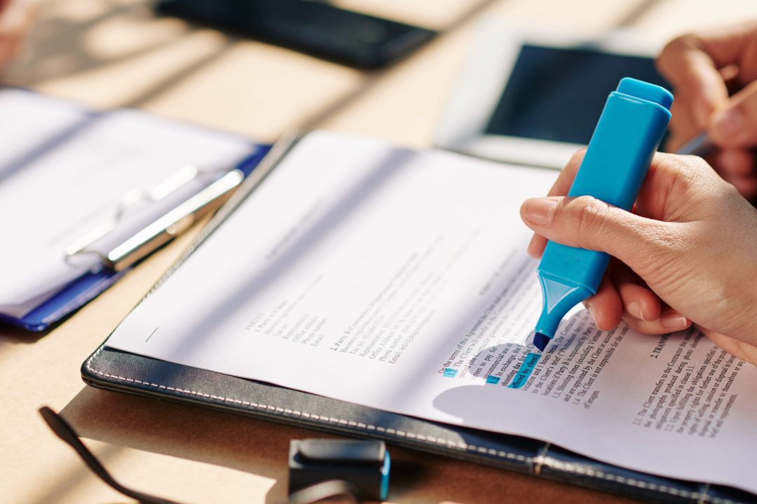 A hand holding a highlighter over a contract