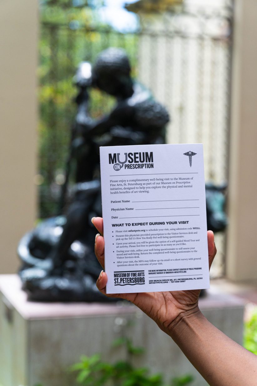 A person holding up a "prescription pad" reading "Museum on Prescription" with a form for the patient's information and things to know about visiting