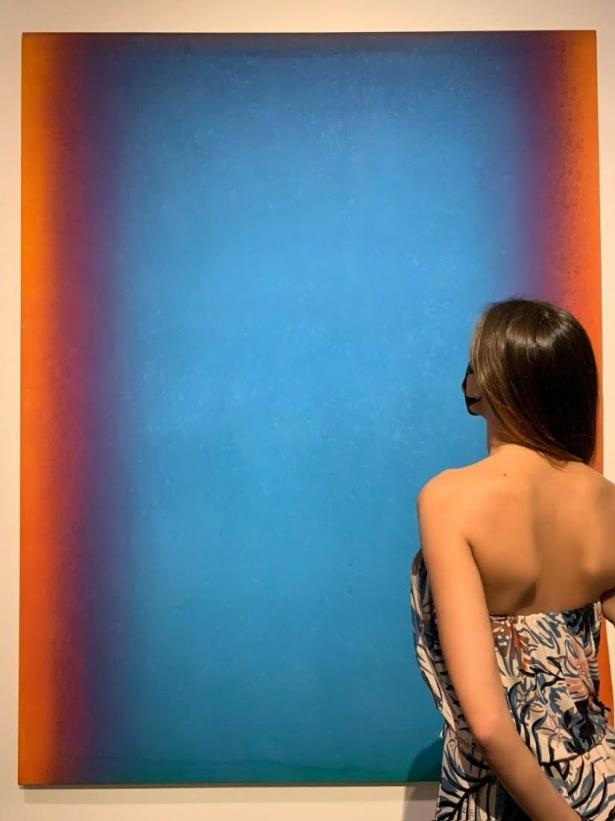 A visitor in front of an abstract painting of a blue field of color with red and dark blue at the edges
