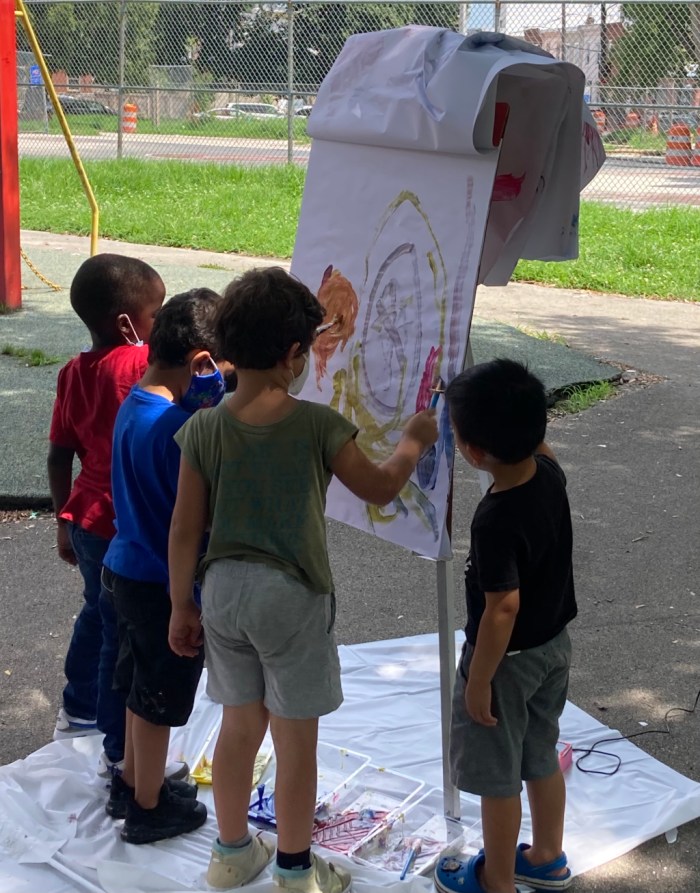 A group of children working on a painting on an easel