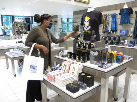 A shopper carrying a Museum Store Sunday tote bag and browsing a display of Ruth Bader Ginsburg merchandise