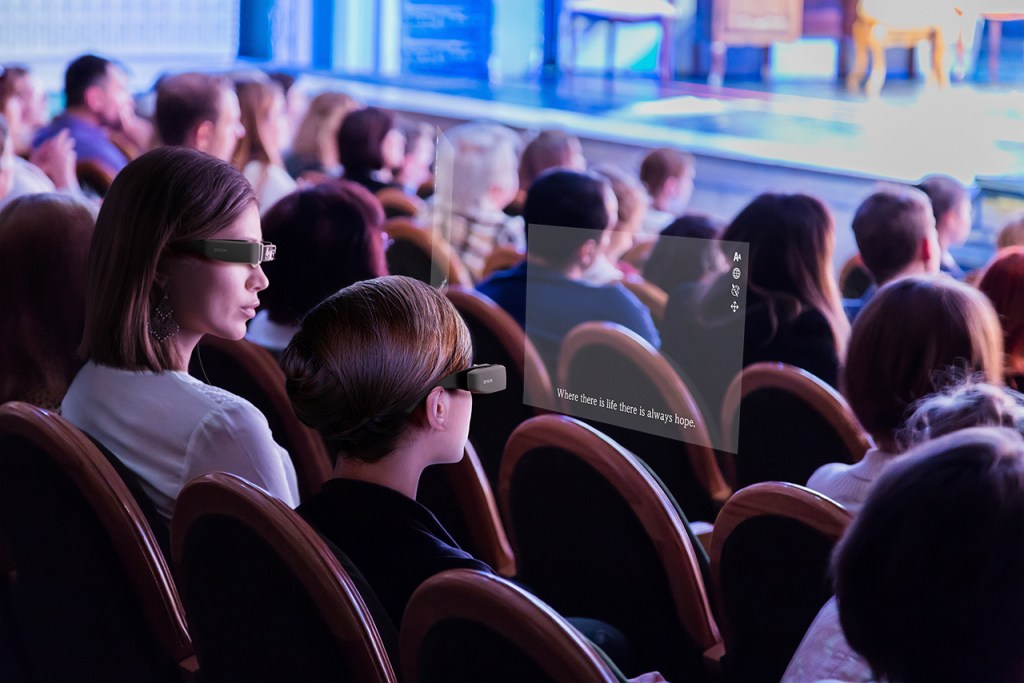 Two audience members at a play wearing digital glasses which superimpose captions over their vision