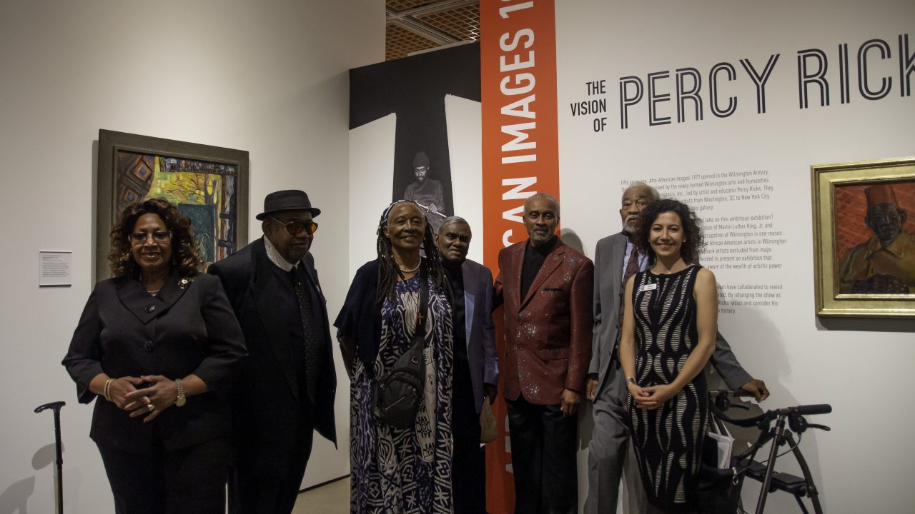 A group of people posing with a museum staff member wearing a badge at the entrance to a museum exhibition