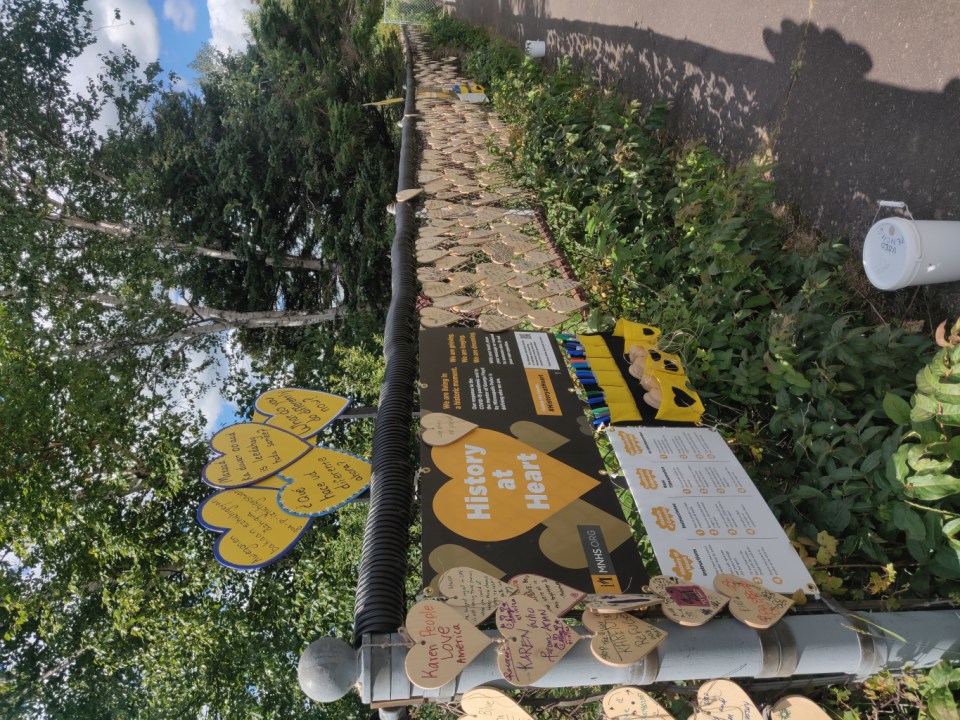 The start of a chainlink fence with a sign reading "History at Heart" and prompts in multiple languages, plus a stock of blank hearts and markers to complete the activity.