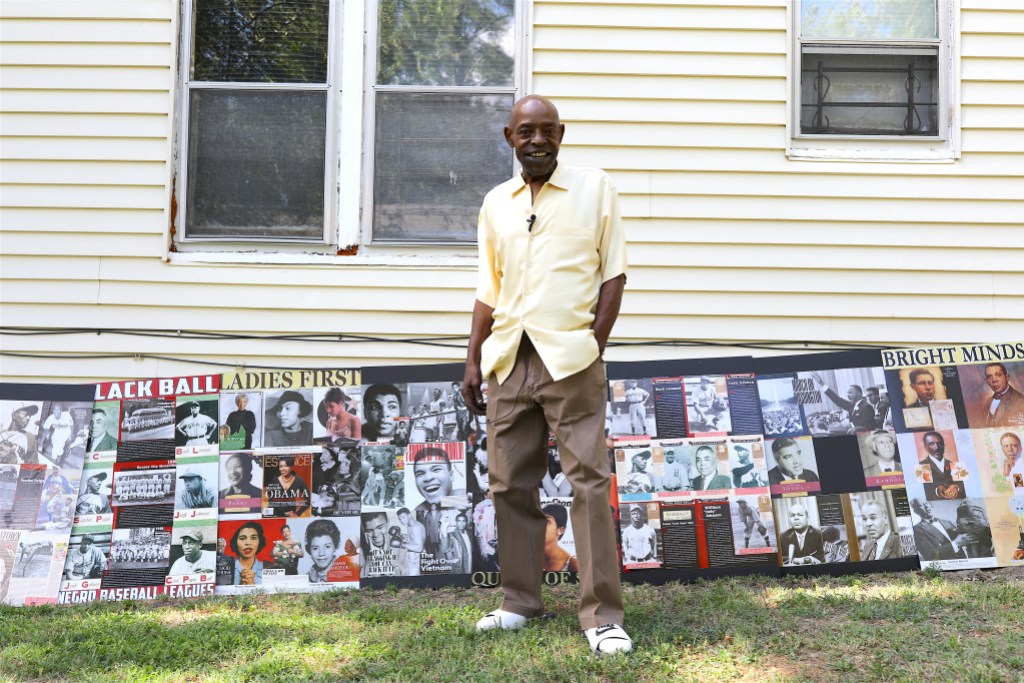 A person posing with a collage of historical images from Black history in front of a home