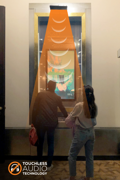 Two people looking at a display with a rendering of a sound beam emitting from a speaker above their heads