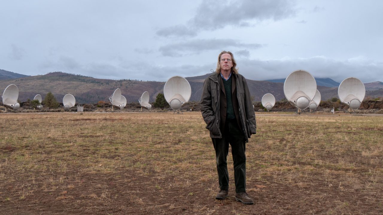 A person standing in a field in a mountainous landscape surrounded by satellite dishes