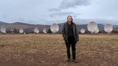 A person standing in a field in a mountainous landscape surrounded by satellite dishes