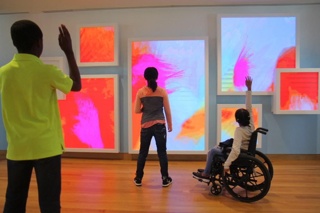 Children playing in front of an interactive game on a wall, one of whom uses a wheelchair