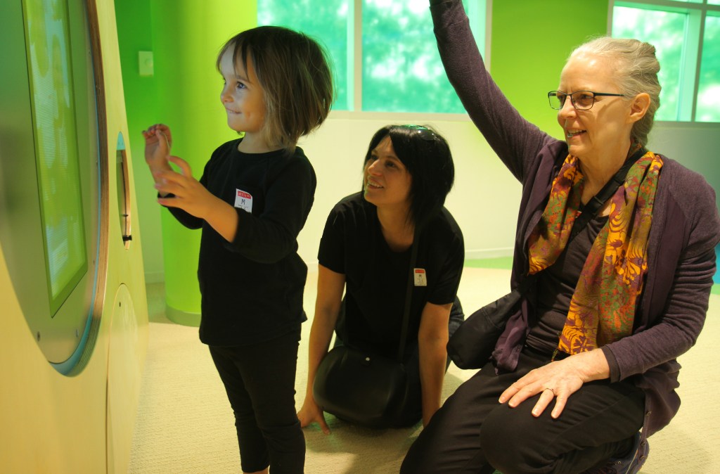 Two adult guardians with a child playing in front of an interactive game