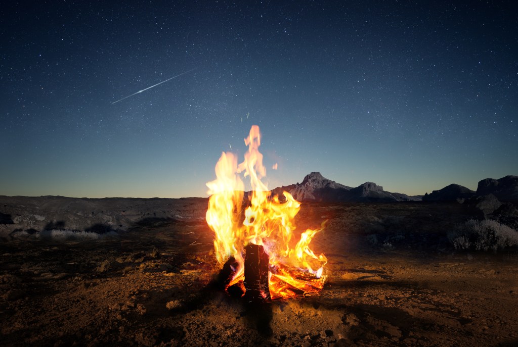 A campfire under the stars in a rocky landscape