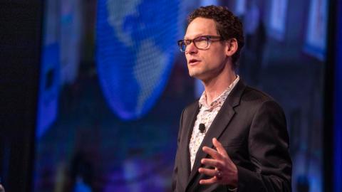 Jake Barton speaking in front of a screen showing a world map