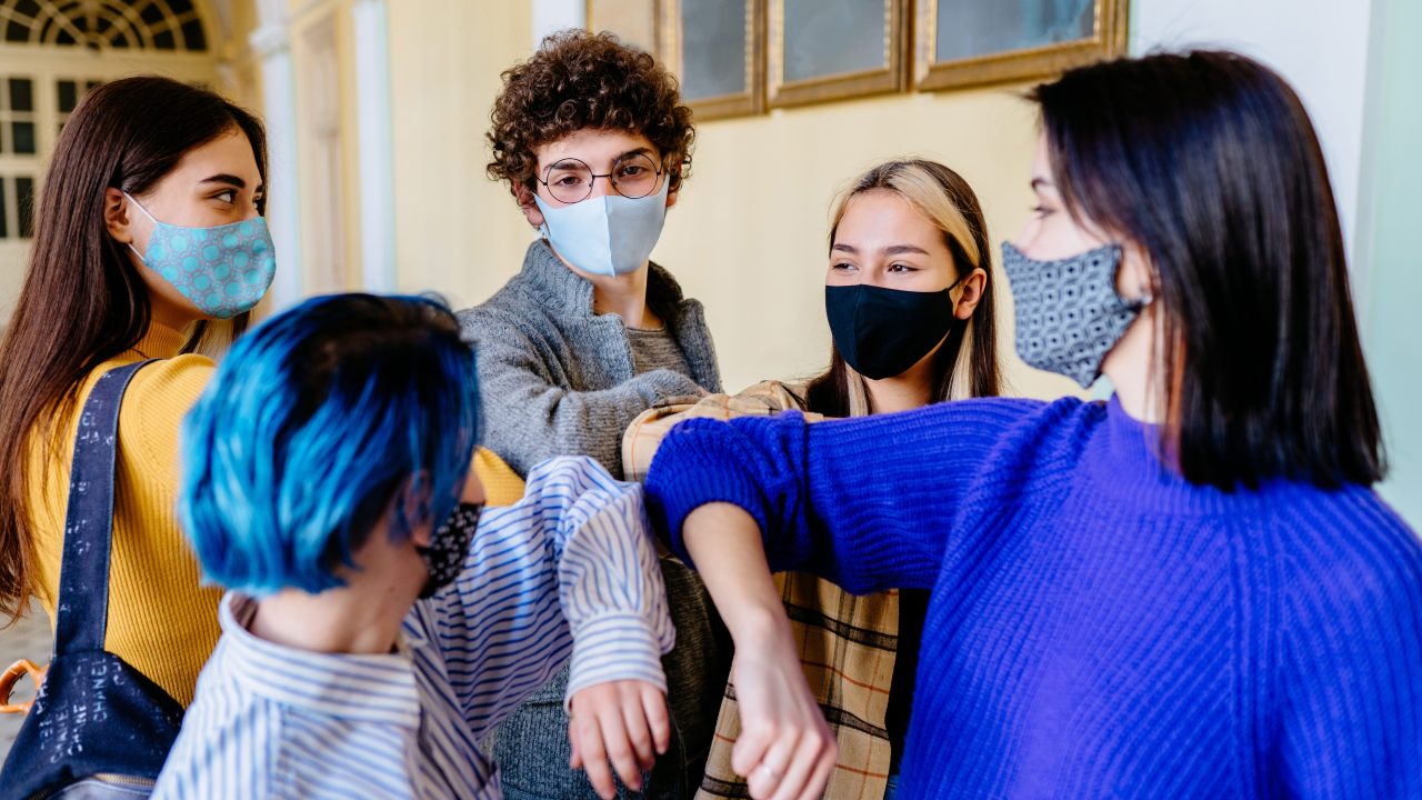 A group of students wearing face masks while bumping their elbows.