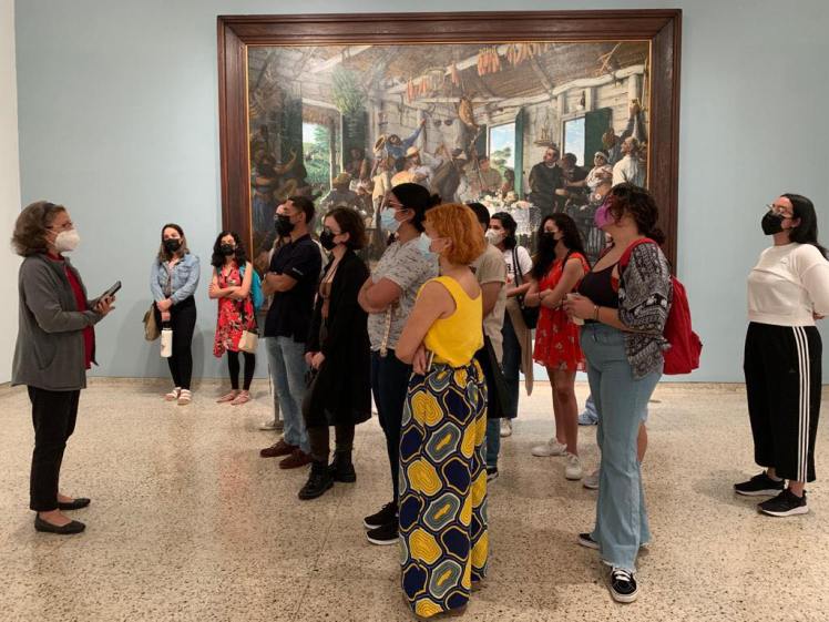 A group of students listening to a museum employee in front of a painting in a museum