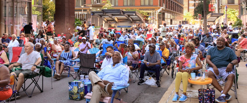 A crowd of people sitting in stadium chairs on a city street