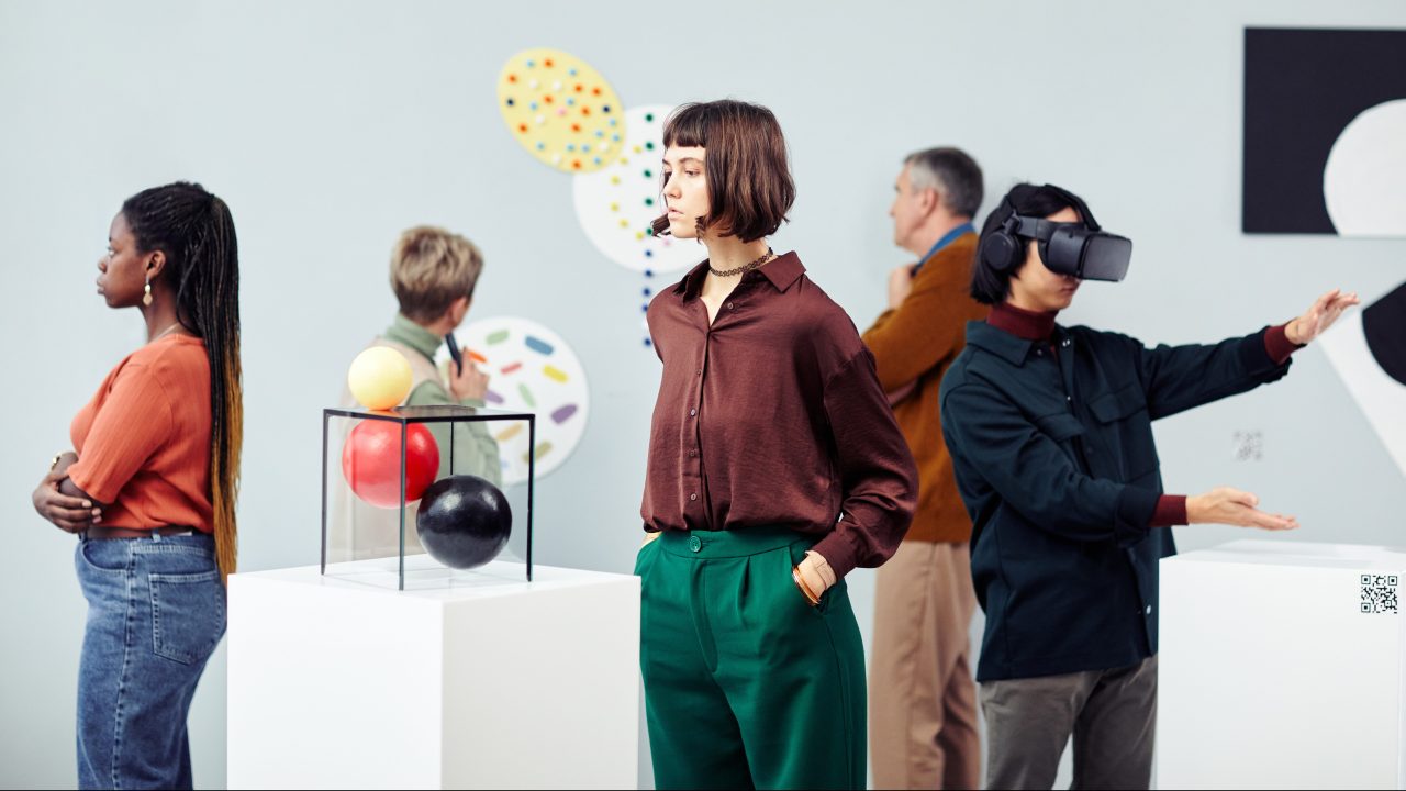 A group of young people looking at objects in a gallery space, with one person wearing a VR headset