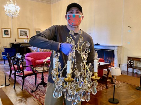 A staffperson wearing a Filoli uniform handling a chandelier with gloves
