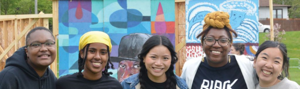 Five people stand smiling at the camera in front of a colorful mural.