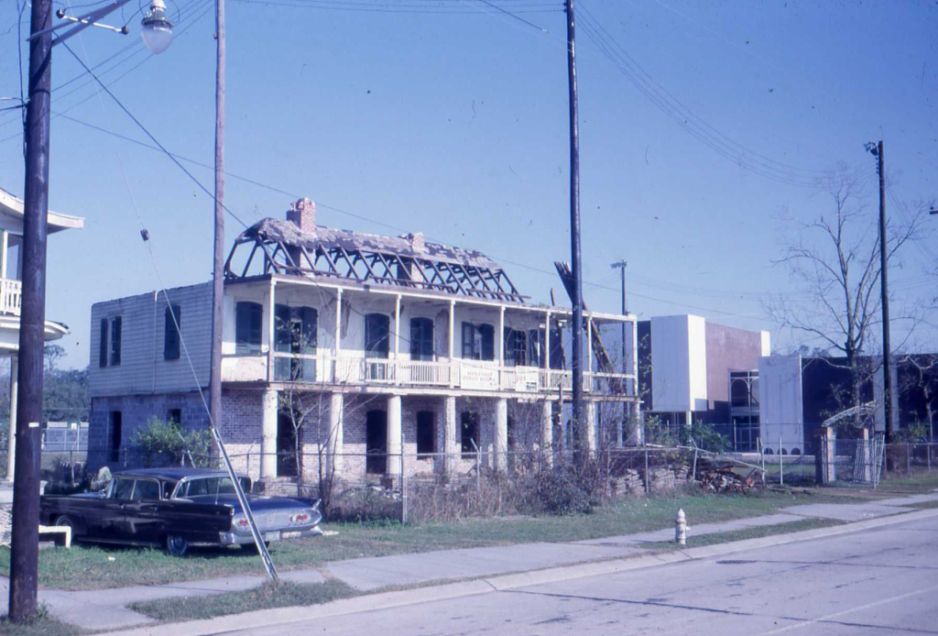 A vintage photograph of a two-story house with the damaged skeleton of a roof on top of it