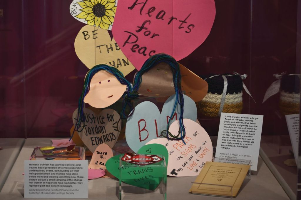 A group of handmade paper art in the shape of hearts sits on a shelf with an interpretive label.