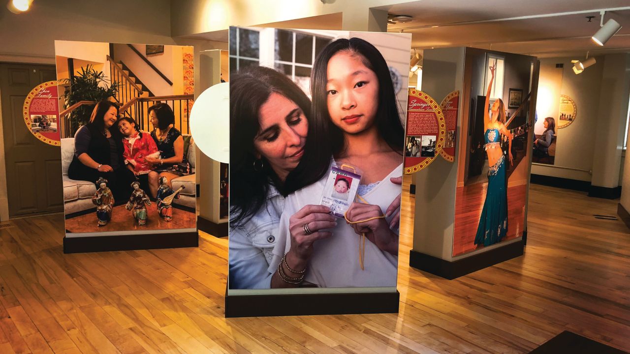 Exhibit panels stand in a gallery each with a larger than life size image of family members.