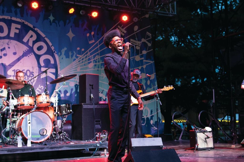 A person stands on a stage singing with a band behind them. 