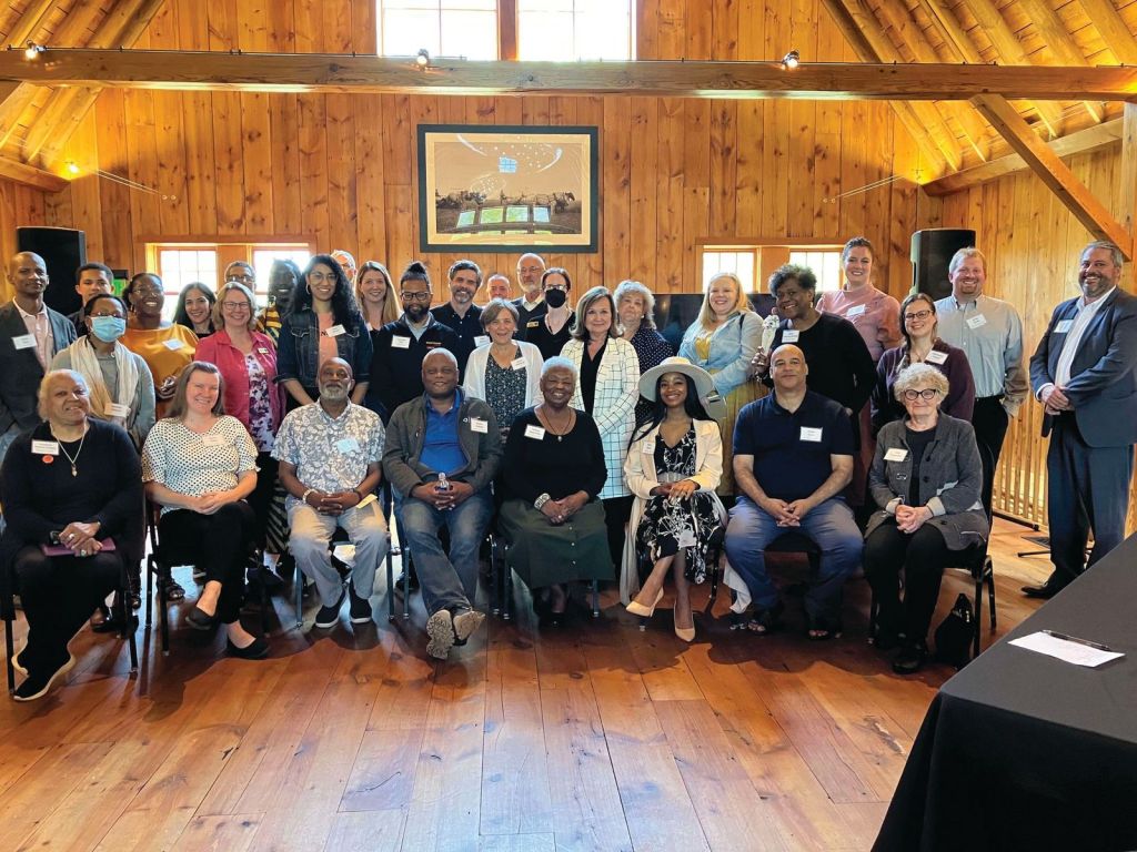 A large group of people pose for a group photo in a room with wooden cladding. 