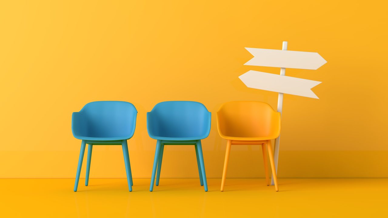 Three chairs, two blue and one yellow, next to a direction sign with arrows pointing two ways