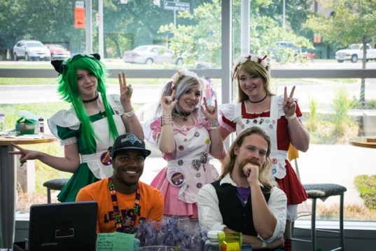 A group of people in anime-style maid costumes posing with people in a lobby